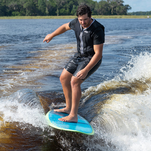 Man wearing black wetsuit riding a blue Boss Hoss V2 5'4" foiling board on a lake with greenery in the background