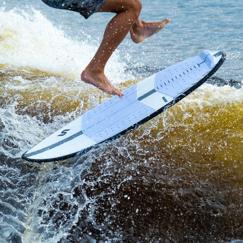 Athlete performing a jump on water using a white and black Coaster V6 foil board with a textured surface, showcasing rider-driven design and One-Lock modular system.