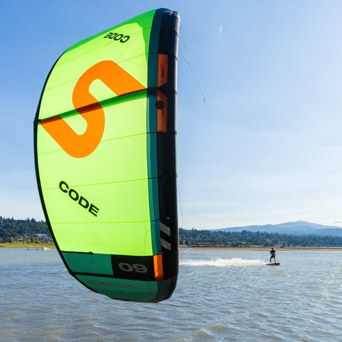 Rider using the bright green and orange Code V2 kite on the water during a clear day, showcasing smooth freeride performance and intuitive handling in a scenic outdoor setting.