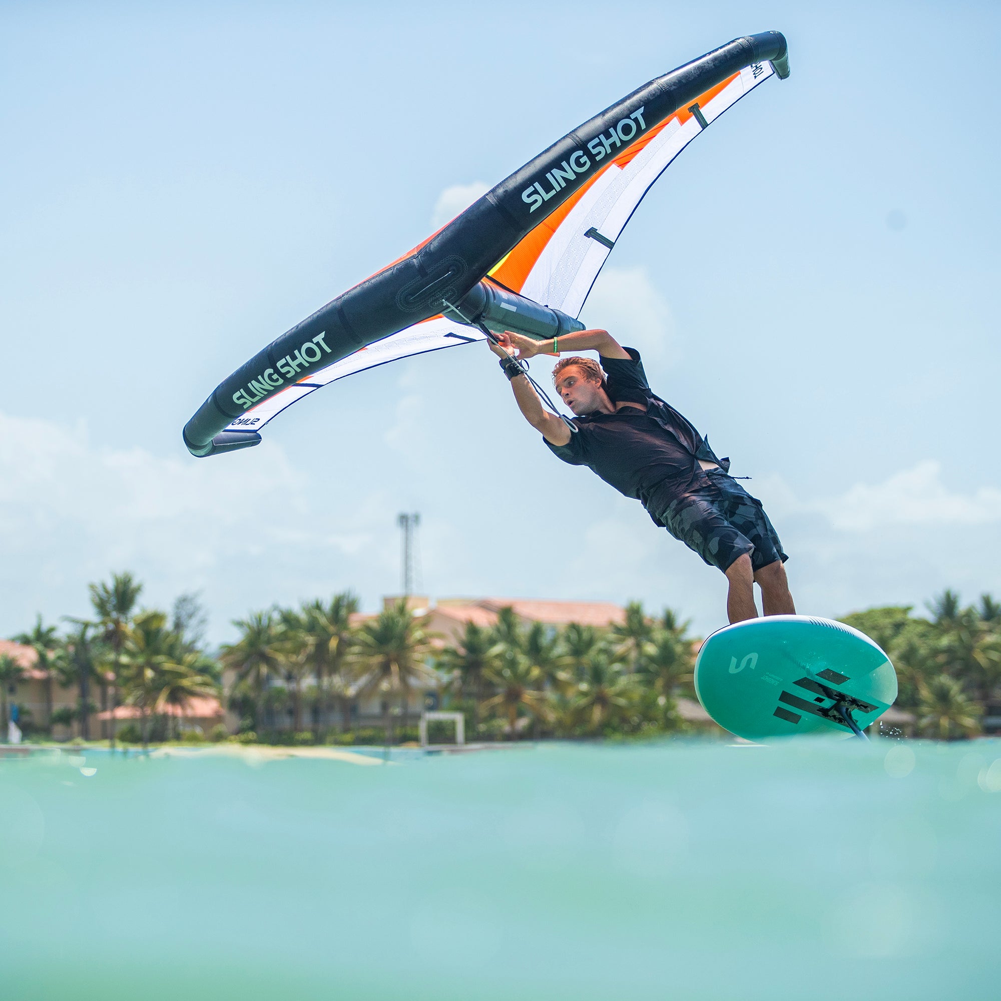 Athlete riding a foil board over water using a black, white, and orange wing with "One-Lock Wing QuickStart Package" branding, demonstrating a one-lock modular foil system.